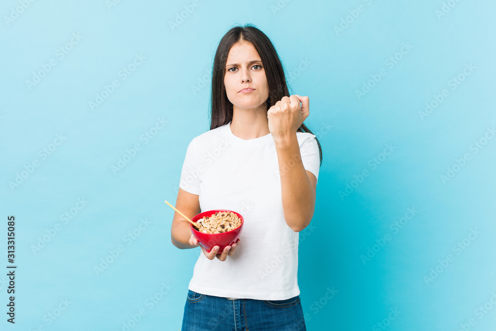 Young caucasian woman holding a cereals bowl showing fist to camera, aggressive facial expression. Young caucasian woman holding a cereals bowl showing fist to camera, aggressive facial expression.