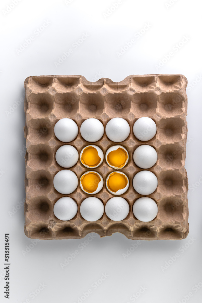 top view photo of raw chicken eggs on recyclable cardboard tray, four broken with yolk on the top, paper packaging pattern with copy space on white background top view photo of raw chicken eggs on recyclable cardboard tray, four broken with yolk on the top, paper packaging pattern with copy space on white background