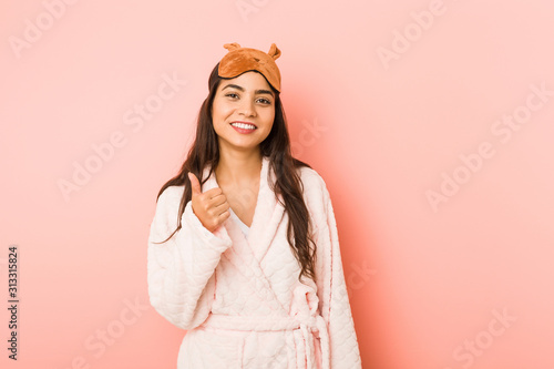 Young indian woman wearing a pajamas and sleep mask isolated smiling and raising thumb up