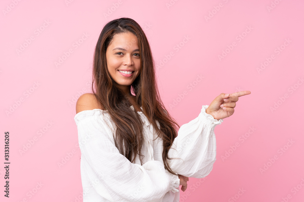 Young Brazilian girl over isolated pink background pointing finger to the side