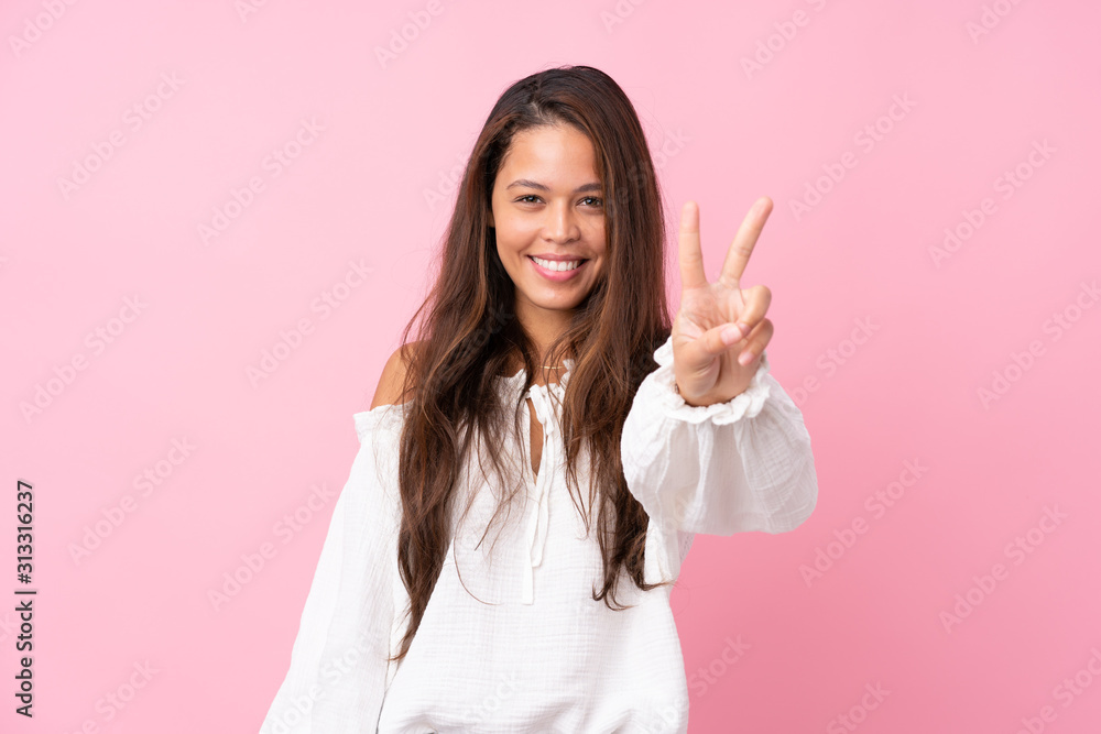 Young Brazilian girl over isolated pink background smiling and showing victory sign Young Brazilian girl over isolated pink background smiling and showing victory sign