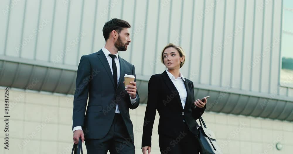 Caucasian young good looking businessman and businesswoman walking down the stairs in the morning with coffee while going to work and discussing plans for a day. Caucasian young good looking businessman and businesswoman walking down the stairs in the morning with coffee while going to work and discussing plans for a day.