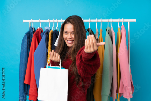 Young Brazilian girl with shopping bag in a store over isolated blue background inviting to come with hand. Happy that you came