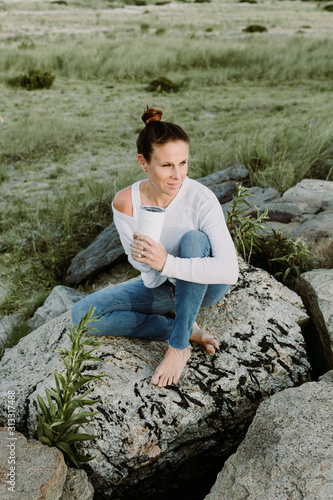 Young Woman Sitting On A Rock Holding A Cup  Relaxed Yoga Lifestyle Concept