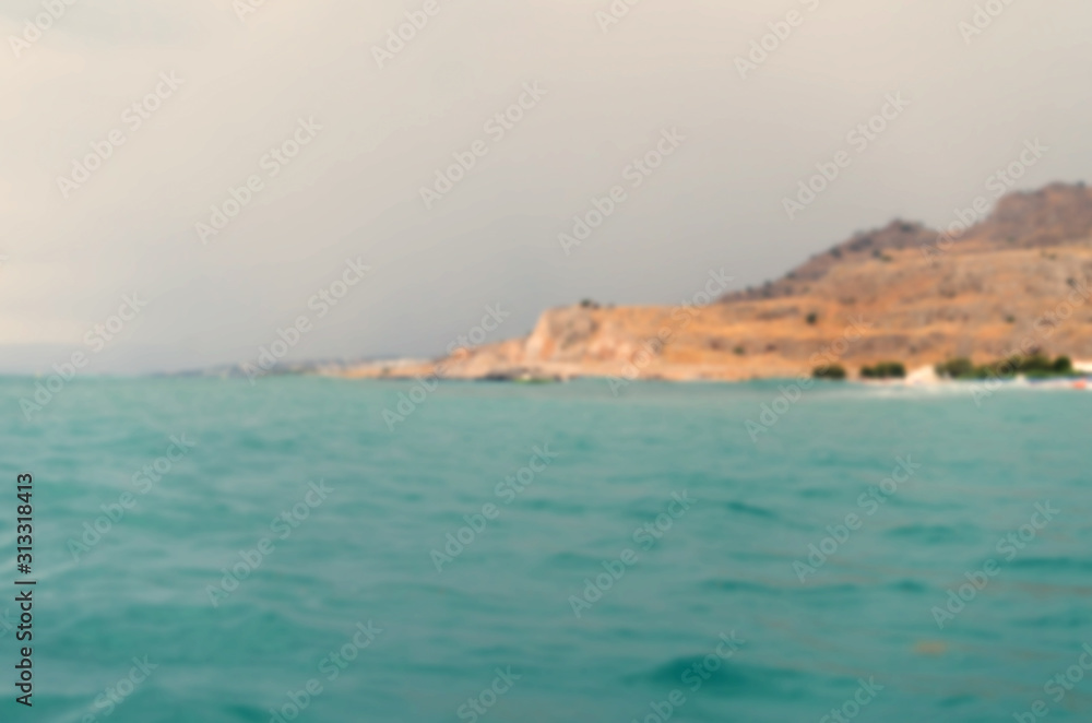Defocused sea and gloomy sky above the mountains of Rhodes. Blurred seashore of Lardos (Rhodes, Greece) for design purposes