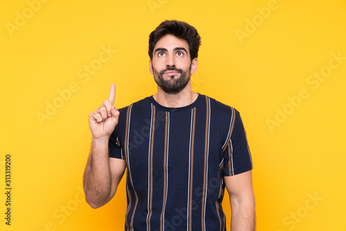 Young handsome man with beard over isolated yellow background pointing with the index finger a great idea