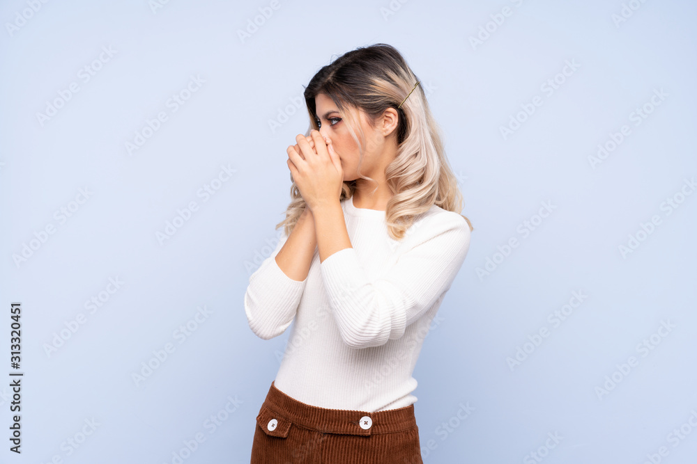 Young teenager girl over isolated blue background covering mouth and looking to the side Young teenager girl over isolated blue background covering mouth and looking to the side