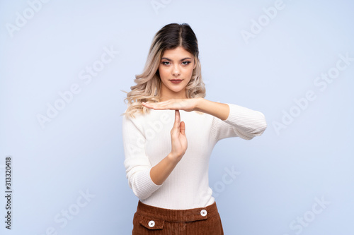 Young teenager girl over isolated blue background making time out gesture