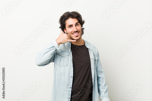 Young handsome man against a white background showing a mobile phone call gesture with fingers.