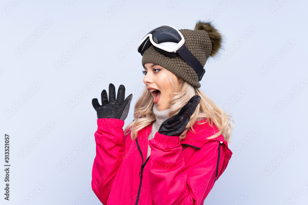 Skier teenager girl with snowboarding glasses over isolated blue background with surprise facial expression Skier teenager girl with snowboarding glasses over isolated blue background with surprise facial expression