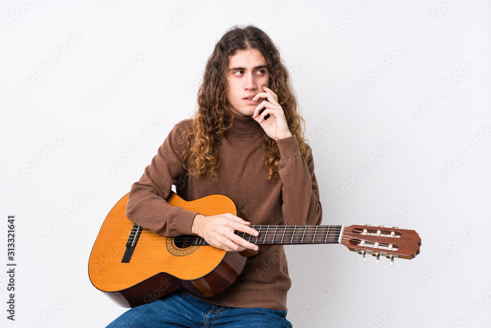 Young caucasian man playing guitar isolated relaxed thinking about something looking at a copy space. Young caucasian man playing guitar isolated relaxed thinking about something looking at a copy space.