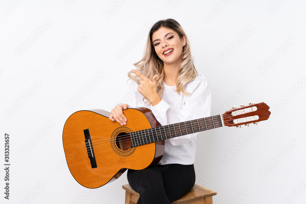 Teenager girl with guitar over isolated white background pointing to the side to present a product Teenager girl with guitar over isolated white background pointing to the side to present a product