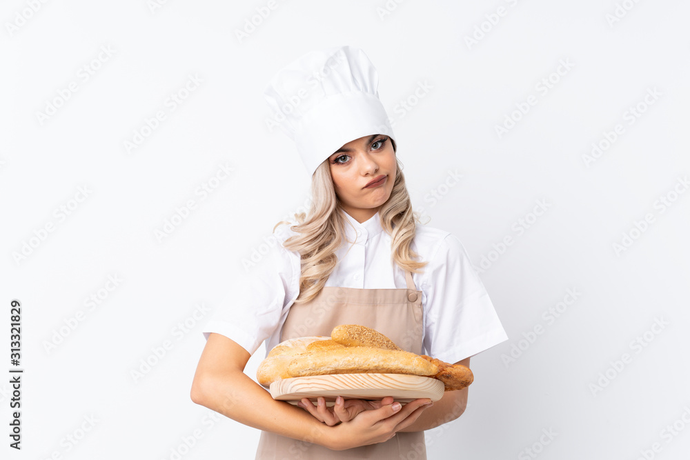 Teenager girl in chef uniform. Female baker holding a table with several breads over isolated white background keeping arms crossed Teenager girl in chef uniform. Female baker holding a table with several breads over isolated white background keeping arms crossed