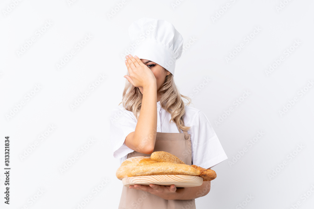Teenager girl in chef uniform. Female baker holding a table with several breads over isolated white background covering eyes and looking through fingers Teenager girl in chef uniform. Female baker holding a table with several breads over isolated white background covering eyes and looking through fingers