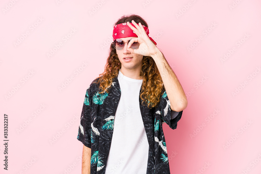 Young long hair hippie man posing in a pink background excited keeping ok gesture on eye. Young long hair hippie man posing in a pink background excited keeping ok gesture on eye.