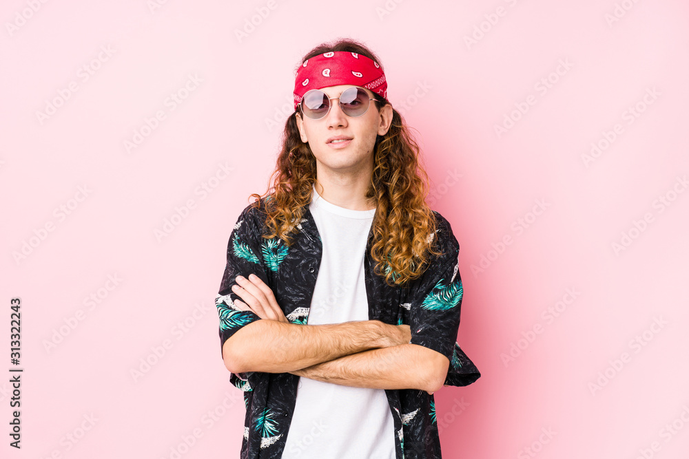 Young long hair hippie man posing in a pink background who feels confident, crossing arms with determination.
