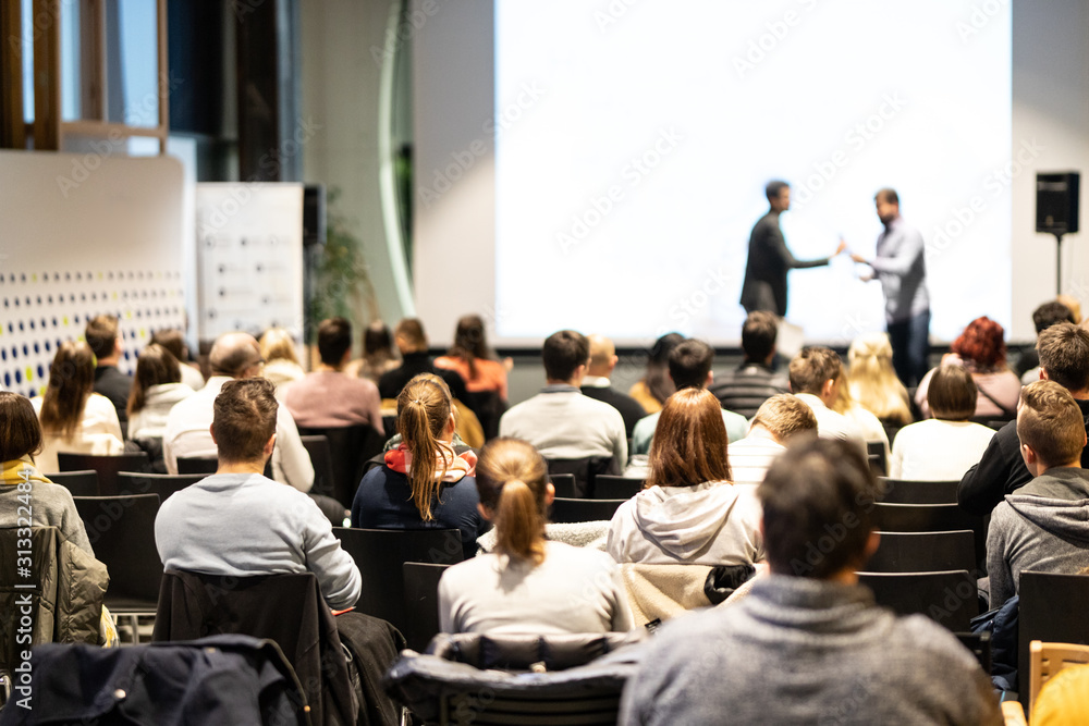 Fototapeta premium Startup team giving a pitch deck presentation in conference hall at business event. Audience at the conference hall. Business and Entrepreneurship concept. Focus on unrecognizable people in audience.