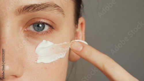 Young woman puts a white cream on her face