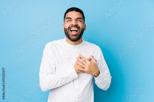 Young latin man against a blue background isolated laughing keeping hands on heart, concept of happiness.