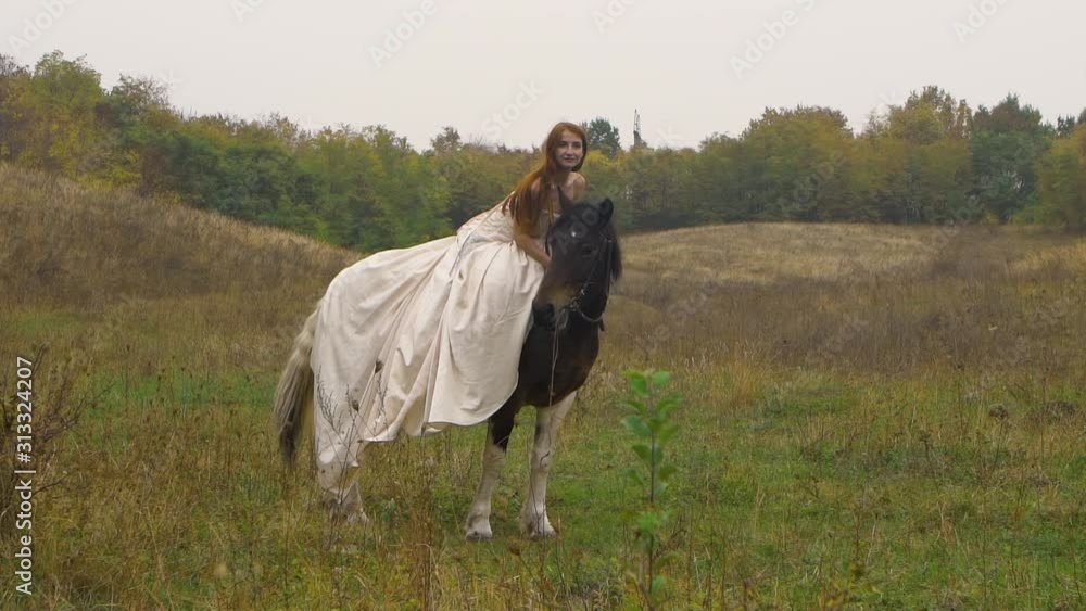 Red-haired horsewoman in poofy dress is riding horse on field Red-haired horsewoman in poofy dress is riding horse on field
