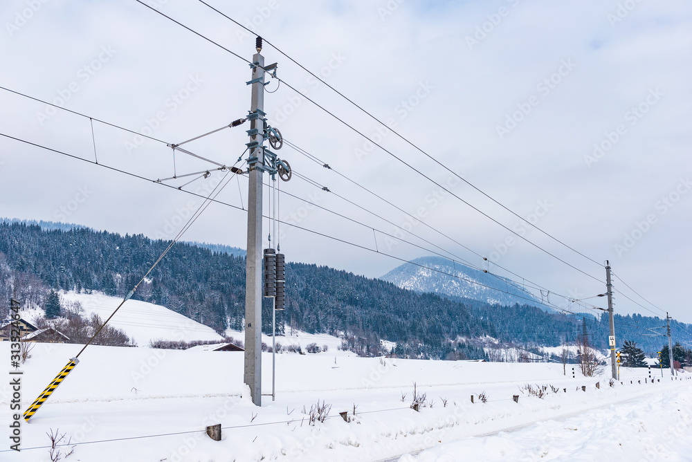Railway electrification system - electric power overhead line network, pylon against cloudy, blue sky and mountains in winter. Railway electrification system - electric power overhead line network, pylon against cloudy, blue sky and mountains in winter.