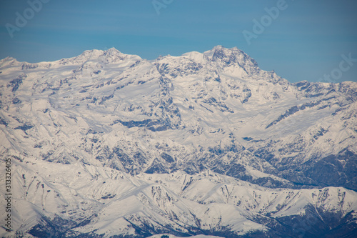 Airplane window photography: overflying the alps, snowy mountains view from above. Blue sky. © laura