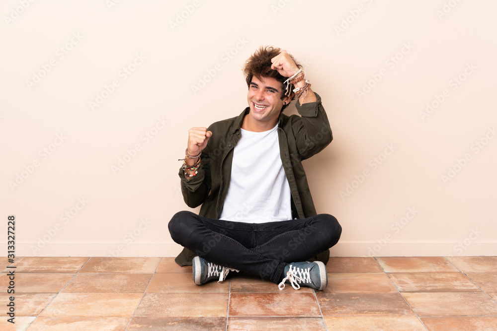 Young caucasian man sitting on the floor celebrating a victory Young caucasian man sitting on the floor celebrating a victory
