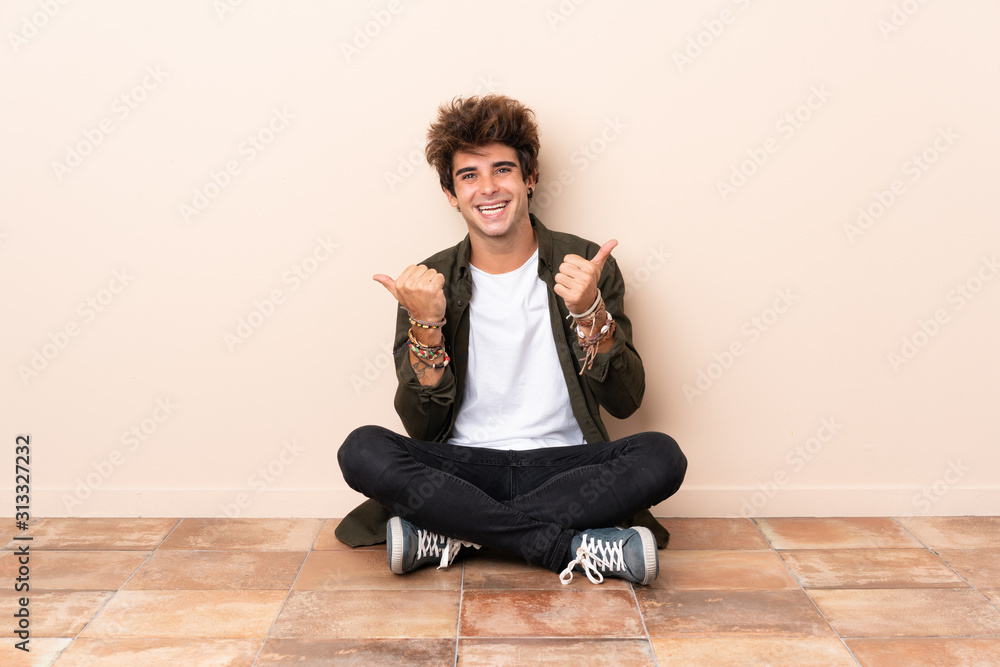 Young caucasian man sitting on the floor with thumbs up gesture and smiling Young caucasian man sitting on the floor with thumbs up gesture and smiling