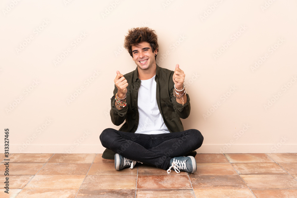 Young caucasian man sitting on the floor making money gesture Young caucasian man sitting on the floor making money gesture