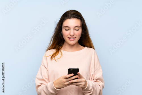 Young brunette girl over isolated blue background sending a message or email with the mobile