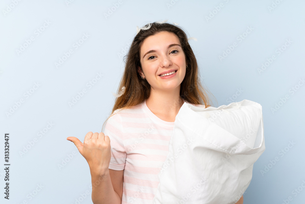 Young woman in pajamas over isolated blue background pointing to the side to present a product Young woman in pajamas over isolated blue background pointing to the side to present a product