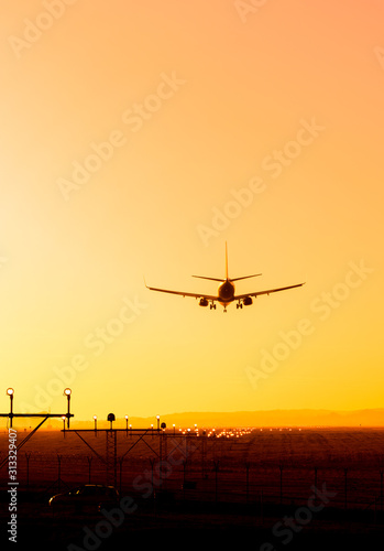 Back view silhouette of airplane landing at the airport at sunny orange and purple sunset. Runway end identification lights and strobe glowing.
