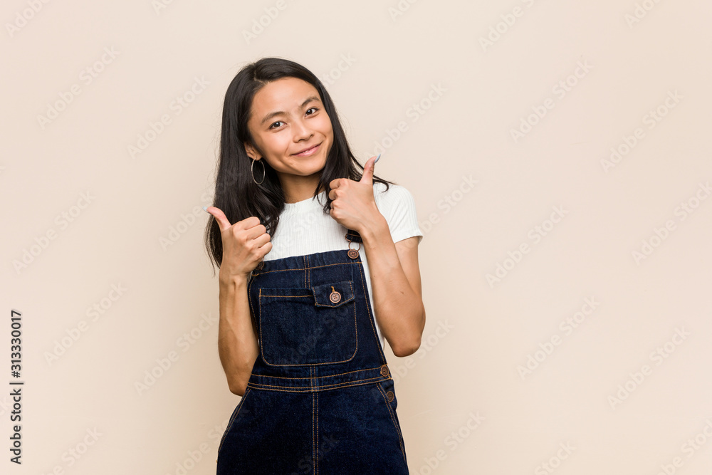 Young cute chinese teenager Young blonde woman wearing a coat against a pink background raising both thumbs up, smiling and confident. Young cute chinese teenager Young blonde woman wearing a coat against a pink background raising both thumbs up, smiling and confident.