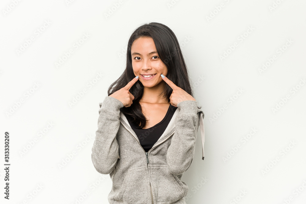 Young fitness chinese woman smiles, pointing fingers at mouth. Young fitness chinese woman smiles, pointing fingers at mouth.