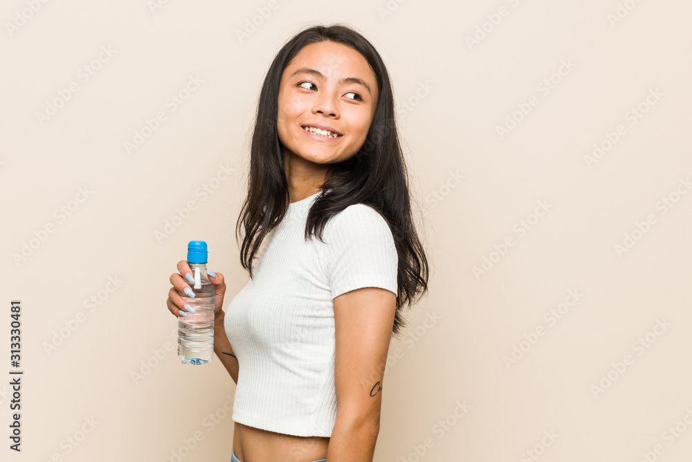 Young asian woman holding a water bottle looks aside smiling, cheerful and pleasant. Young asian woman holding a water bottle looks aside smiling, cheerful and pleasant.