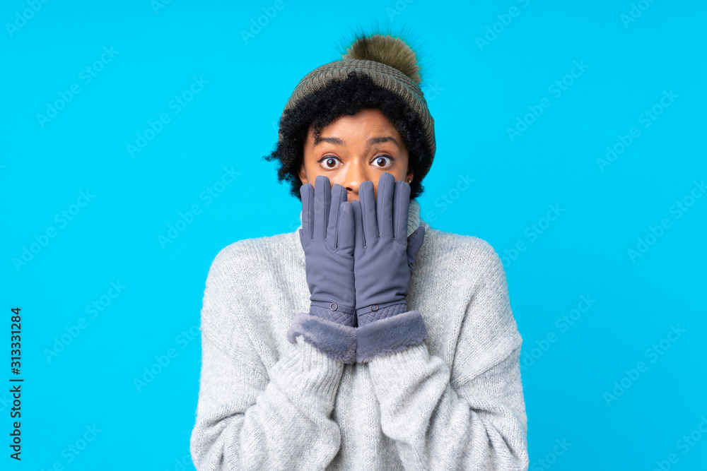 African american woman with winter hat over isolated blue background with surprise facial expression African american woman with winter hat over isolated blue background with surprise facial expression