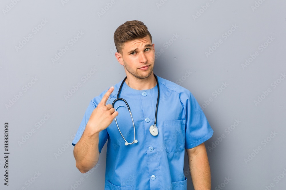 Young nurse man pointing with finger at you as if inviting come closer.