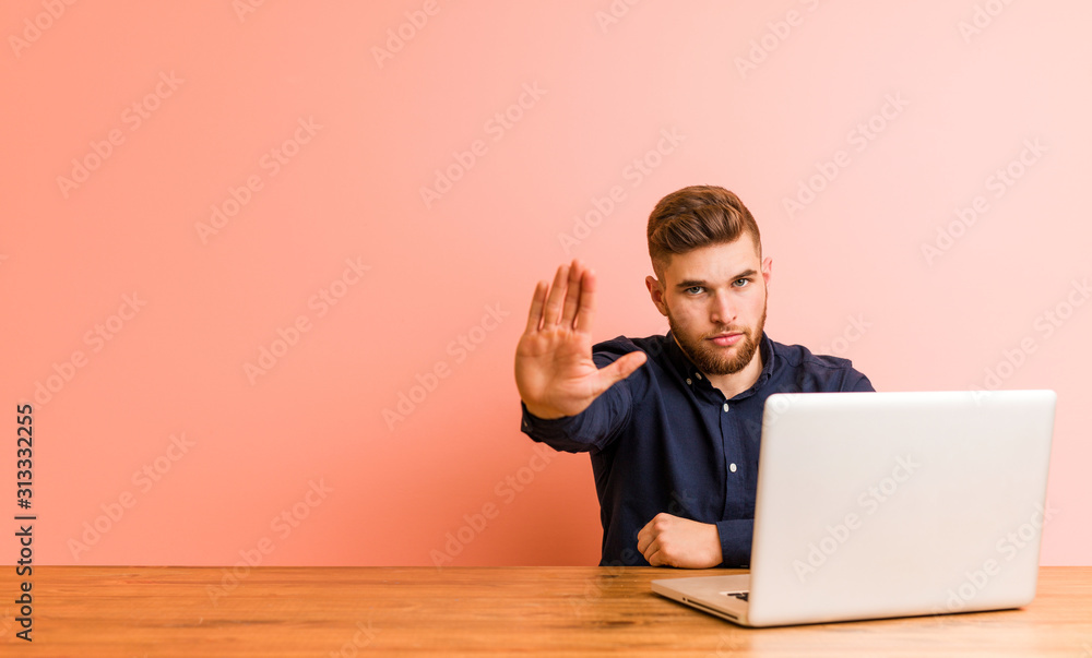 Young man working with his laptop standing with outstretched hand showing stop sign, preventing you. Young man working with his laptop standing with outstretched hand showing stop sign, preventing you.