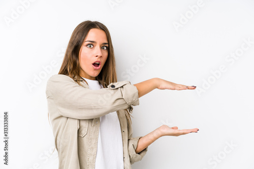 Young caucasian woman  isolated shocked and amazed holding a copy space between hands.