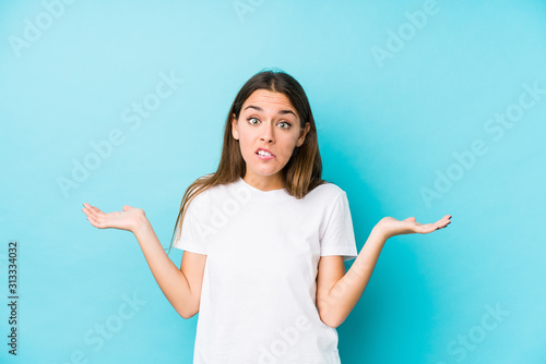 Young caucasian woman  isolated confused and doubtful shrugging shoulders to hold a copy space.