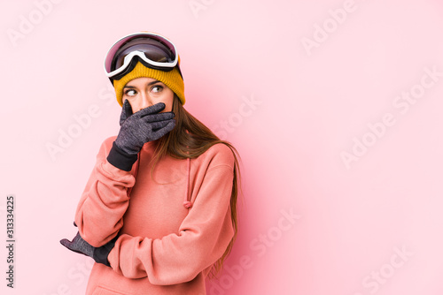Young caucasian woman wearing a ski clothes isolated thoughtful looking to a copy space covering mouth with hand.