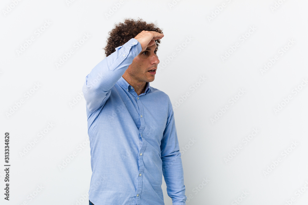 Young curly mature man wearing an elegant shirt looking far away keeping hand on forehead. Young curly mature man wearing an elegant shirt looking far away keeping hand on forehead.