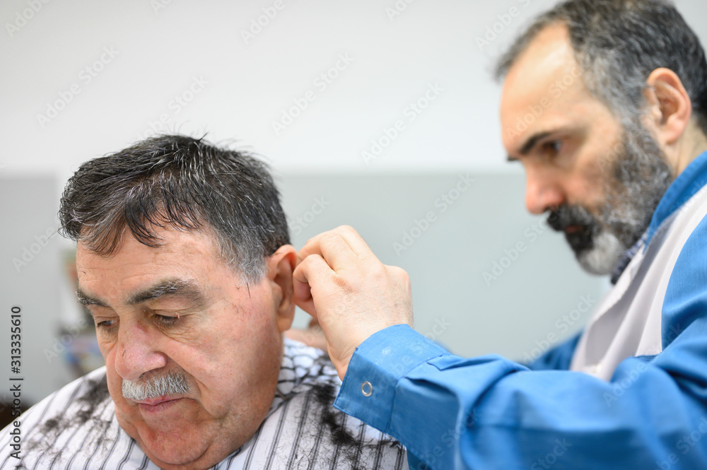 Fototapeta premium Barber trimming hair of old man at barber shop .