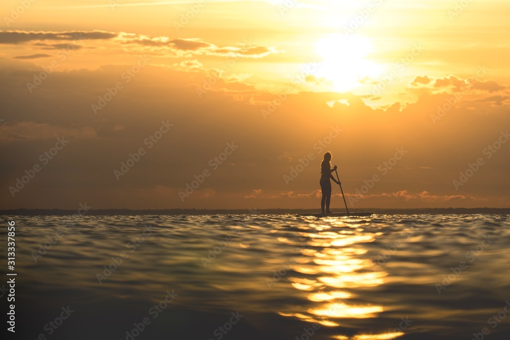 Girl paddlesurfing in sunset.