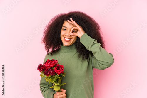 Young afro woman holding a roses isolated Young afro woman holding a rosesexcited keeping ok gesture on eye.
