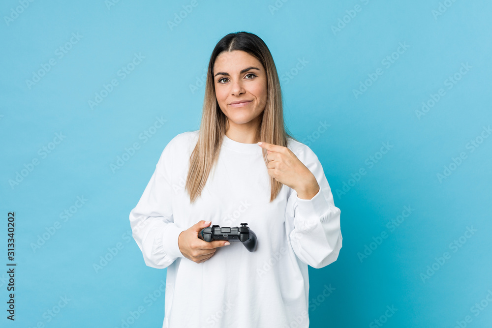 Young caucasian woman holding a game controller pointing with finger at you as if inviting come closer. Young caucasian woman holding a game controller pointing with finger at you as if inviting come closer.