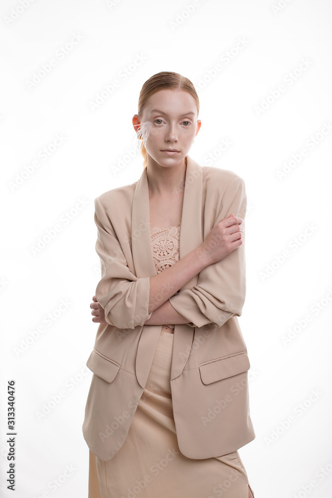 Young blonde model with art makeup posing in beige skirt suit in white studio Young blonde model with art makeup posing in beige skirt suit in white studio