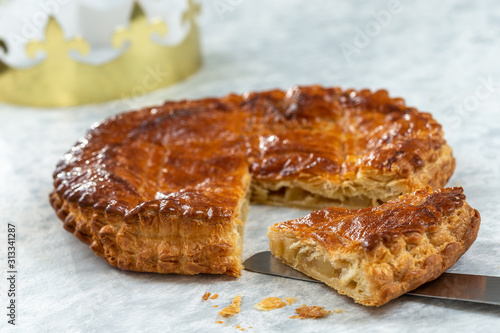 Epiphany Twelfth Night cake french galette des rois made of puff pastry, slice apart with the charm inside, open crown leaning beside