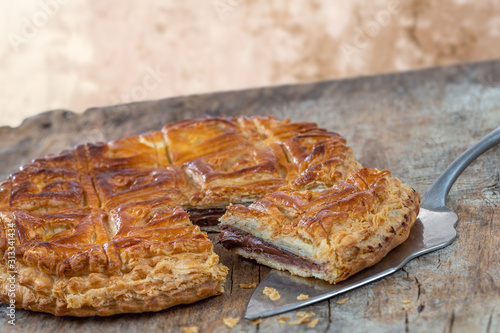 Epiphany Twelfth Night cake french galette des rois made of chocolate puff pastry, slice apart with the charm on wooden background photo