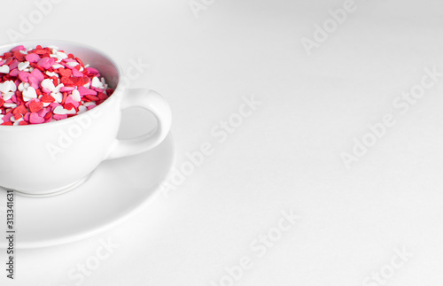 white cup of coffee on a white background filled with heart shaped confetti. selective focus. valentine day concept.